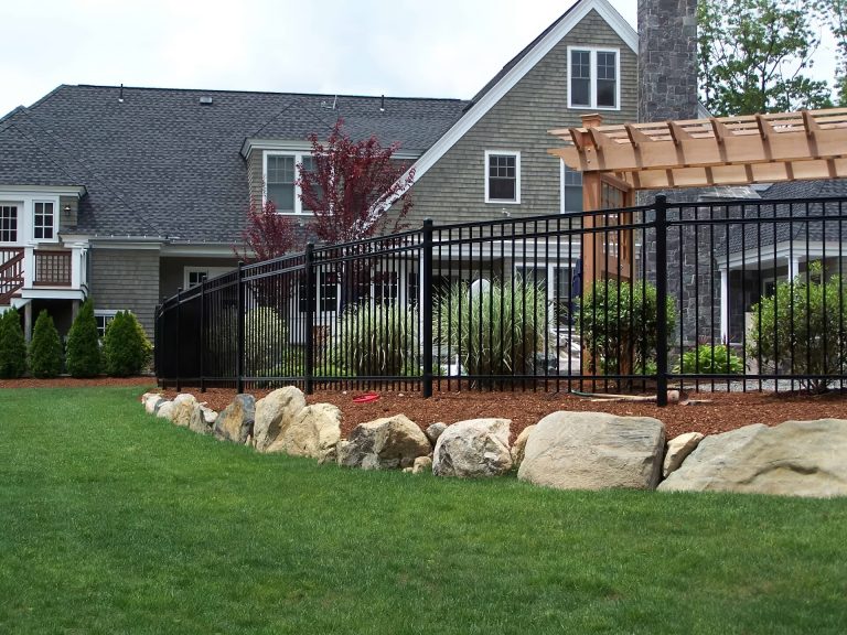 A stone fence with grass in front of a house, showcasing residential services by Premier Outdoor Solutions.